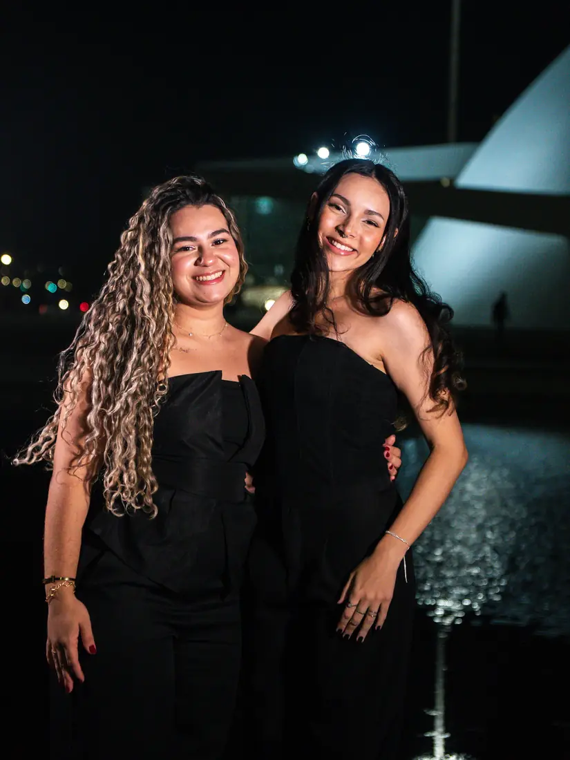 Duas formandas de vestido preto abraçadas